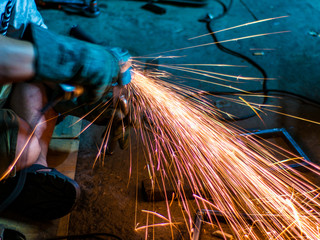 Worker using grinder to refine metal bar in workshop 