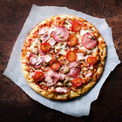 Fresh italian pizza with mushrooms, ham, tomatoes, cheese on on backing paper, dark background. Copy space. Homemade with love. Fast delivery. Recipe and menu. Top view. Square.