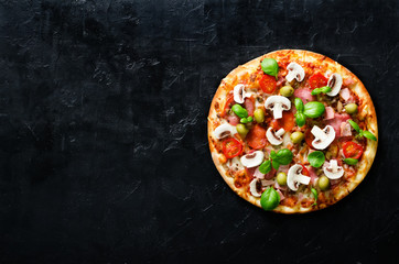 Fresh italian pizza with mushrooms, ham, tomatoes, cheese, olive, basil on black concrete background, rustic table. Copy space. Homemade with love. Fast delivery. Recipe and menu. Top view