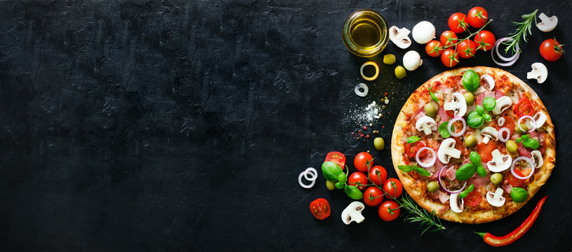 Food ingredients and spices for cooking mushrooms, tomatoes, cheese, onion, oil, pepper, salt, basil, olive and delicious italian pizza on black concrete background. Copyspace. Top view. Banner.