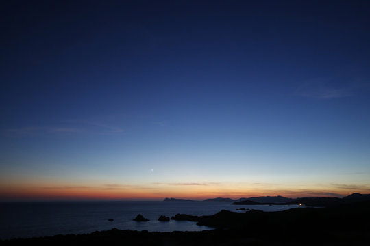 Foto di cielo blu al tramonto sopra un mare blu scuro. In lontananza si vede l'orizzonte