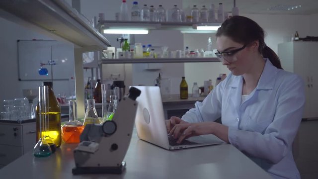 Portrait adult caucasian doctor working with laptop in laboratory. Chemist engineer or lab technician entering data on laptop. Professional woman working in the evening alone.