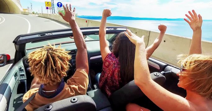 Back view of friends waving arms driving in convertible, color graded