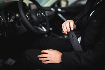 Close-up of man sitting in car fastening seat belt