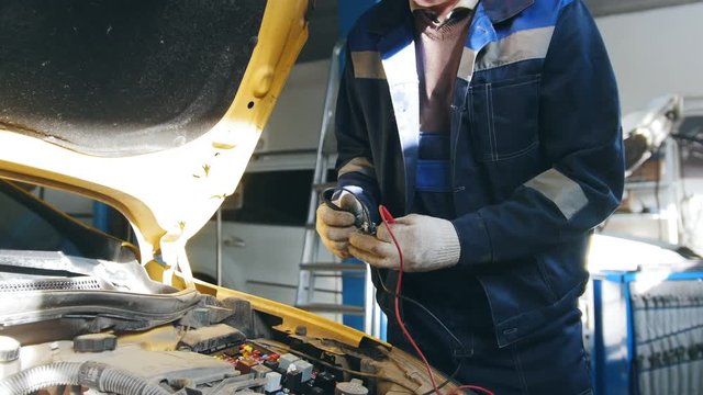 Male mechanic in gloves checks electric components in hood of the car - automobile service diagnostics