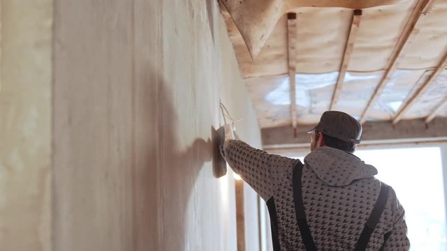 Caucasian middle-aged male worker wearing peaked cap using palette knife in slowmotion
