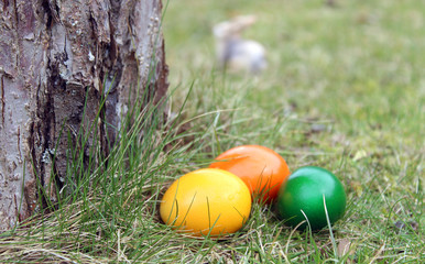 Colored Easter eggs lying beside a tree, with Easter bunny in background