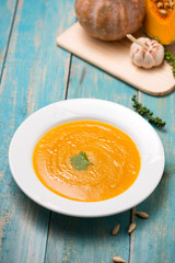  Top view of pumpkin and carrot soup with cream and parsley on blue  wooden background.