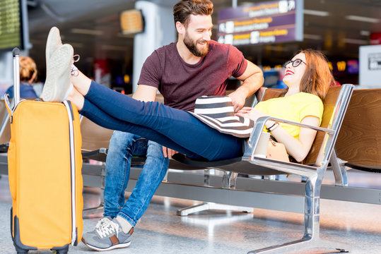Young couple in colorful t-shirts sitting with baggage at the waiting room of the airport