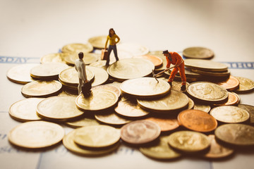 Miniature people work on coins used for business concept