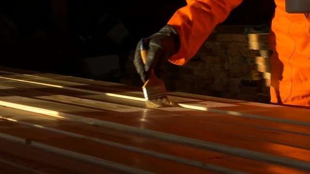 Impregnation and imbibition of diagonally arranged wooden bars with a brush. Construction and painting works from wood. Varnishing and gloss of wood in the shop. Sun glares.