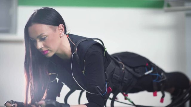 Girl lying in the palm, and raises the body rises in the bar. Striking a woman connected to the electrical stimulator - a modern form of training and fitness EMC. Woman with piercings doing fitness