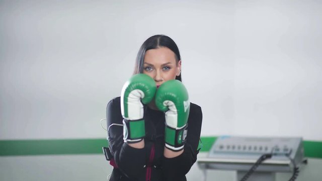 Spectacular brunette simulates shot of green boxing gloves. Woman boxing during EMC training. Woman engaged in fitness EMC.