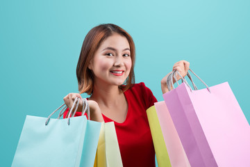 Beautiful young asian woman with colored shopping bags over blue background