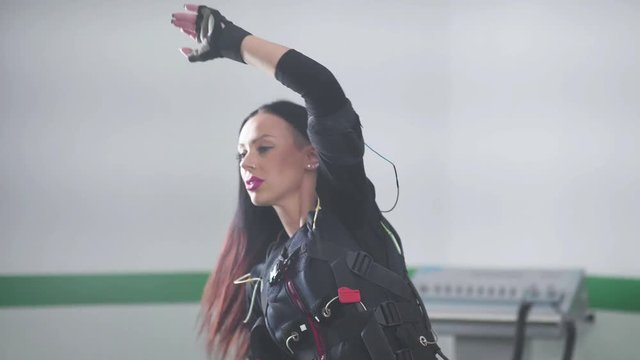 EMS fitness: woman crouches and makes a tilt to the side connected to the sensors, electrical muscle. Electrical stimulation of muscles during training.