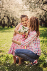 Fototapeta premium spring vertical portrait of happy mother and kid daughter on the walk in blooming cherry garden.