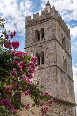 Fototapeta na wymiar Ancient stone bell tower in Hum, croatian town, the smallest in the world. Beautiful red flowers and ancient fortress tower on background.