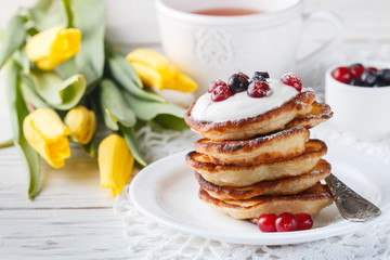 Breakfast. Fritters with sour cream and fresh berries. Pancakes. A Cup of tea, cranberries, black currant and flowers on the table. Selective focus