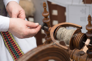Hands of woman in action spinning line flax with a spinning wheel 
