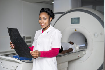 Doctor Holding X-ray While Patient Lying On CT Scan Machine