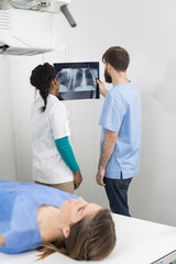 Radiologists Analyzing X-ray With Woman Lying In Foreground