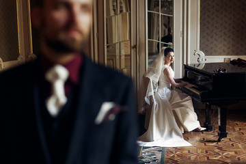 elegant gorgeous bride playing the fortepiano and stylish handsome groom posing in rich old room....