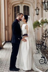 Naklejka premium elegant gorgeous bride and stylish groom hugging kissing, sensual touch on background of old building. unusual luxury wedding couple in retro style.