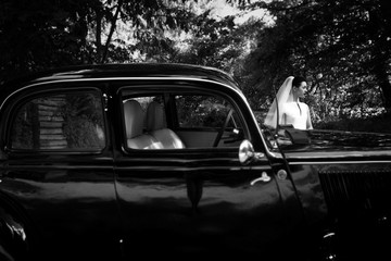 elegant gorgeous bride on background of stylish black car. luxury wedding in retro style. black white photo