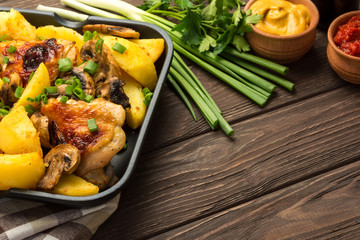 Dinner with baked chicken legs with olives spiced with aromatic herbs and potatoes with mushrooms on a rustic background.  Copy space.
