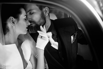 luxury elegant wedding couple kissing and embracing in stylish black car. gorgeous bride and handsome groom in retro style. romantic moment black white photo