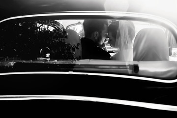 luxury elegant wedding couple embracing in stylish black car in light. unusual view from back. gorgeous bride and handsome groom in retro style. black white photo - Powered by Adobe