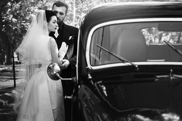 luxury elegant wedding couple embracing at stylish black car in light. gorgeous bride and handsome groom in retro style. black white photo