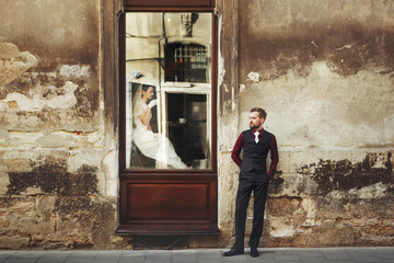 elegant gorgeous bride  drinking coffee in window and stylish groom posing at building in street outdoors cafe. unusual luxury wedding couple in retro style. romantic moment.