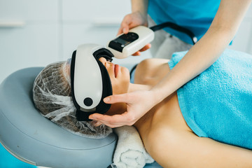 Close up of lying young woman with closed eyes receiving electroporation facial therapy at beauty...