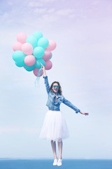 Beautiful young woman with colorful balloons on sky background