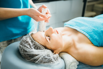 Obraz na płótnie Canvas Hands of beautician squeeze the body cream standing near young woman lying on a massage table in healthy beauty spa salon interior.