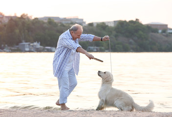 Senior man training dog on riverside