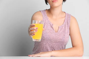 Young beautiful woman with glass of orange juice, on light background