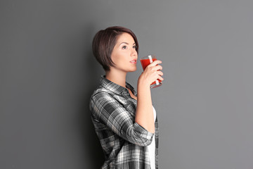 Young beautiful woman with glass of tomato juice, on grey background