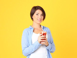 Young beautiful woman with glass of tomato juice, on yellow background