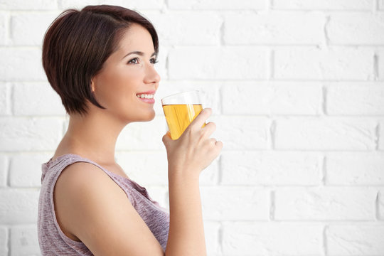 Young beautiful woman with glass of apple juice, on brick wall background