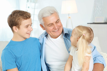 Cute children with grandfather sitting on sofa in living room