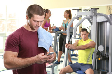 Fototapeta na wymiar Young handsome man with cellphone in gym
