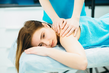 Obraz na płótnie Canvas Young woman lying vestured turquoise towel while massage therapist massaging her shoulders