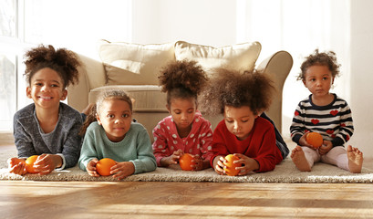 Five cute African girls with oranges lying on floor