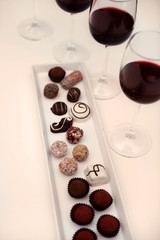 Delicious chocolates and glasses of wine on white table