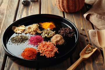 Plate with different spices on wooden background