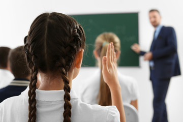 Fototapeta premium Schoolgirl raising hand for answer during lesson