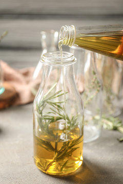 Pouring oil into bottle with rosemary on table