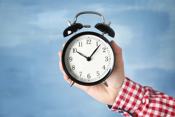 Woman holding vintage alarm clock on color background